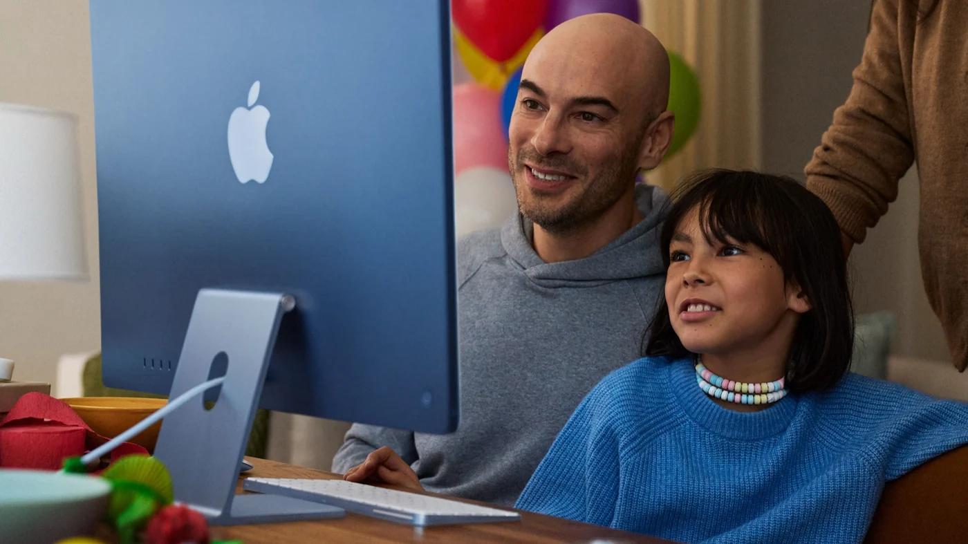 A child uses iMac while adults supervise.