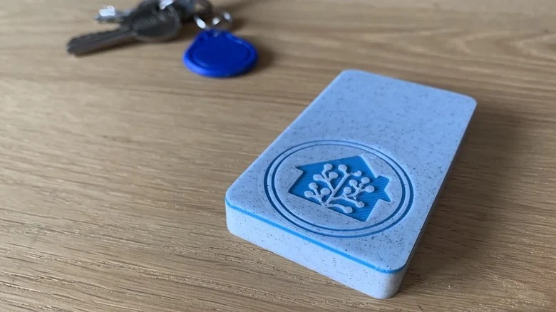 A Home Assistant NFC reader sits on a wooden table beside keys and an NFC key fob.