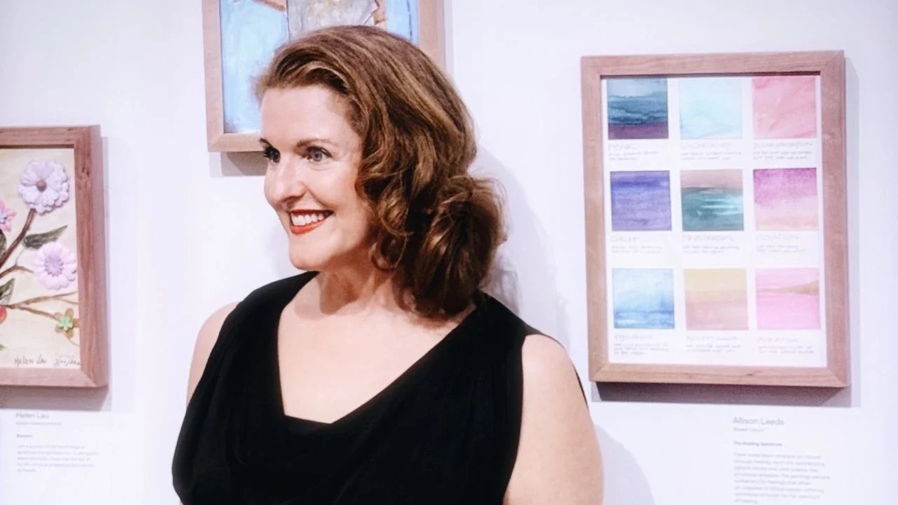 Allison Leeds standing beside framed artwork.