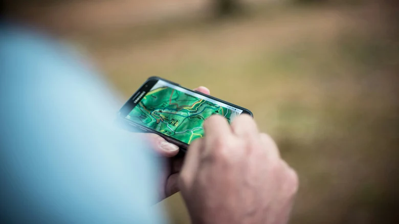 Person holding Samsung Galaxy Android smartphone while hiking with GPS onscreen.