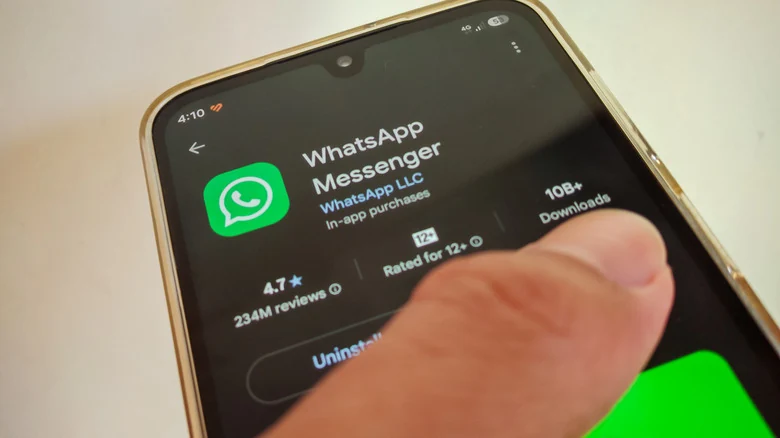 A thumb tapping on the screen of an Android phone showing WhatsApp on the Google Play Store.