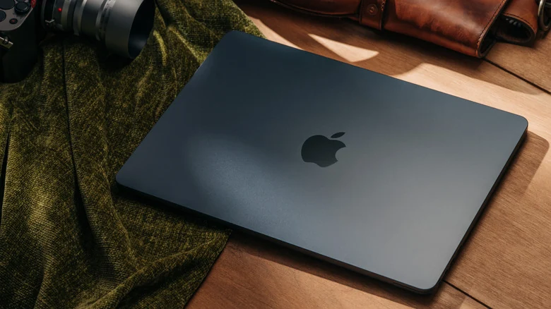 A MacBook Air on a wooden table, surrounded by a camera and leather accessories.